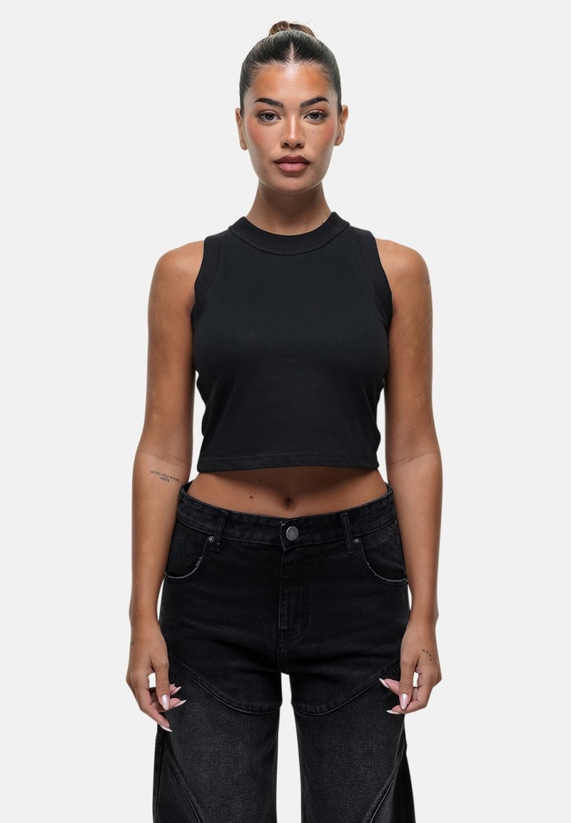 Top nero corto senza maniche con scollatura rotonda, abbinato a jeans neri a vita alta con cuciture visibili e cuciture laterali.