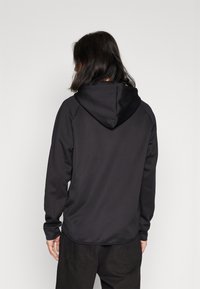 Sudadera negra hecha de un tejido suave, con capucha ajustable, mangas largas y un dobladillo ligeramente redondeado. Sin patrones o detalles visibles.