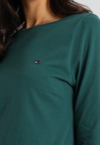 Groene katoenen T-shirt met lange mouwen, voorzien van een klein geborduurd logo in rood, wit en blauw op de linker borst. Regelmatige pasvorm en een gladde textuur.