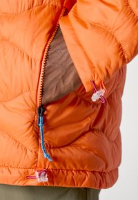 Oranje pufferjack met een gewatteerde textuur, voorzien van een ritszak, verstelbare trekkoorden in blauw en rood, en gemaakt van lichtgewicht materiaal.