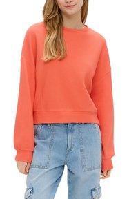 Sweat-shirt boxy corail en tissu texturé avec un col rond, associé à un jean cargo baggy bleu clair. Doté de manches longues et larges.