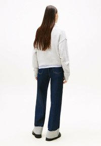 Hellgrauer, übergroßer Pullover mit geripptem Saum; kombiniert mit dunkelblauen, weit geschnittenen Jeans mit ausgefransten grauen Säumen. Lange glatte Haare.