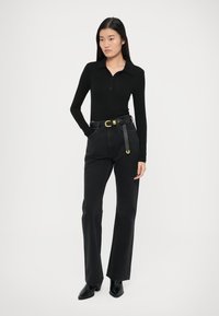 Black fitted long-sleeve polo with a collar, paired with high-waisted black jeans and a wide belt featuring a gold buckle and hardware accents.