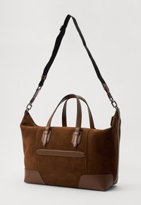 Brun ruskind tote taske med læderdetaljer, dobbelte håndtag og en aftagelig justerbar strop. Har en frontlomme og en struktureret design.