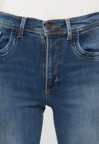 Jeans de denim azul con un ajuste clásico, que presentan detalles cosidos, diseño de cinco bolsillos y un cierre frontal con botón. Tejido texturizado.