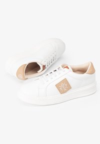 Zapatillas de cuero blanco con una pestaña de talón de ante sintético texturizado en color marrón, suela de goma y un diseño cosido que presenta una insignia con logo cuadrado.