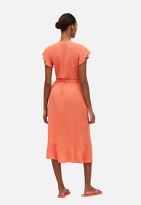 Vestido coral naranja con mangas cortas y ligeramente onduladas, cintura ajustada y dobladillo acampanado. Textura suave con un brillo sutil.