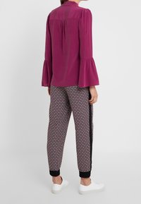 Paarse blouse met uitlopende mouwen en een rugstuk. Patroon sweatpants in zwart en rood met geribbelde boorden, gecombineerd met witte sneakers.