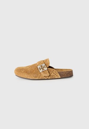 Sabots en daim beige avec un motif de logo embossé, une sangle ajustable et des détails en métal doré. Semelle en liège pour texture et contraste. Design plat.