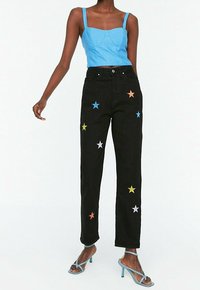 Jeans de denim negros con apliques de estrellas multicolores, corte recto, combinados con un top corto azul y tacones azules con tiras.