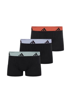 Mannelijk model staat op blote voeten en draagt zwarte boxer briefs met een oranje tailleband met zwarte Adidas-logo's op een effen witte achtergrond.