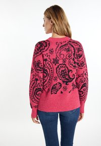Różowy sweter z czarnym wzorem paisley na plecach, prążkowany dół i długie rękawy. Materiał wydaje się być miękki i strukturalny.