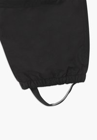 Svart vindjakke med elastisk mansjett på bena og justerbar snorlås. Glatt tekstur med en subtil glans, og har en refleksdetalj i stroppen.
