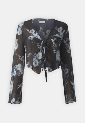 Kukkaprintti crop-top, jossa on läpinäkyvää mustaa kangasta sinisillä ja valkoisilla kukkakuoseilla, pitkät hihat, V-pääntie ja solmittava etuosa.
