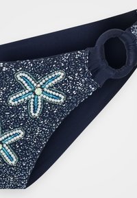 Marinblå bikiniunderdel med intrikata pärldekorationer; har blå och vita blommönster samt en sido-ringdetalj. Slät textur.