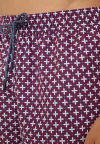 Badehose mit elastischem Bund und Kordelzug, ausgestattet mit einem geometrischen Muster in Rot, Marineblau und Weiß, aus leichtem Material gefertigt.