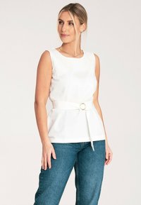 Biała top bez rękawów z marszczoną talią, z okrągłą klamrą paska, w zestawieniu z niebieskimi dżinsami. Gładki materiał, minimalistyczny design.