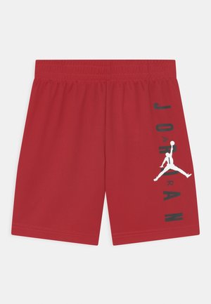 Shorts de sport rouges avec une ceinture élastique, comportant un texte vertical noir "JORDAN" et un logo Jumpman blanc sur la jambe droite.