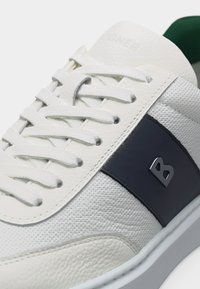 Λευκό δερμάτινο αθλητικό παπούτσι με διάτρητη υφή, λευκά κορδόνια και σκούρο μπλε πλευρικό πάνελ με μεταλλικό λογότυπο γράμματος B.