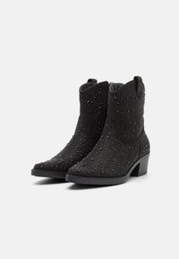 Botines negros con un upper texturizado y acentos de pedrería, puntera puntiaguda y un tacón bajo en bloque para mayor estabilidad.