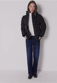 Svart puffjacka med justerbar huva, dragkedjestängning och två framfickor, kombinerad med en vit polotröja och mörk denimjeans.