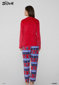 Top rojo de manga larga hecho de material suave, combinado con pantalones de pijama de patrones rojos y azules que presentan personajes de dibujos animados y elementos festivos.