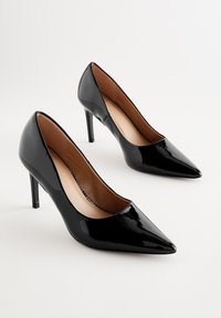 Décolleté nere in vernice con punta appuntita, tacco a spillo e finitura liscia e lucida. Interno con fodera color cuoio.