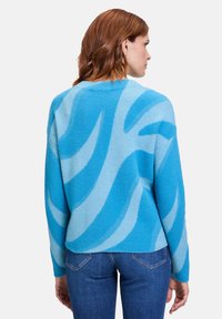 Hellblauer Pullover mit gewellten Mustern in dunklerem Blau. Hergestellt aus einem weichen, strukturierten Stoff, mit überschnittenen Schultern und einem entspannten Schnitt.