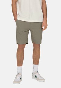 Pantaloni scurți gri deschis cu o croială lejeră, confecționați dintr-un material moale. Purtați cu adidași albi și șosete albe texturate pentru un aspect casual.