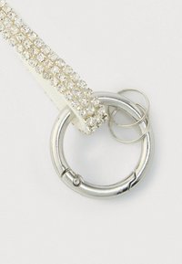 Diržas su sidabrine apdaila iš cirkonių, suapvalintu metaliniu žiedu ir dviem mažais kilpomis; pasižymi sklandžia tekstūra ir blizgiu paviršiumi.