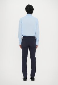 Világoskék, hosszú ujjú ing, tengerészkék, slim-fit nadrág, fekete cipők, hátulról nézve. Sima textúra, letisztult dizájn, minimális részletezés.