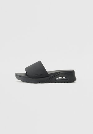 Sandale noire à enfiler avec un dessus en caoutchouc lisse, une large sangle et une semelle extérieure texturée avec un détail de coussin d'air visible sur le côté.