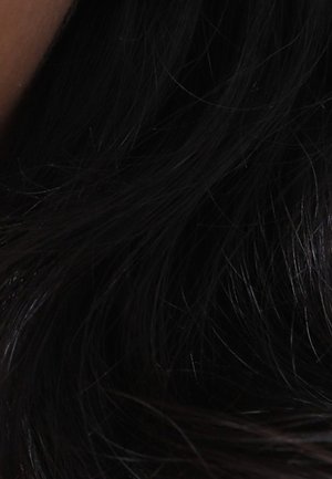 Cheveux longs et foncés avec des ondulations naturelles et lâches couvrant une partie de l'épaule, laissant apparaître une petite section de peau sur le côté gauche.