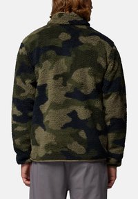 Giacca in pile verde camouflage con superficie testurizzata, colletto alto e design aperto. Presenta toppe scure e una vestibilità rilassata.