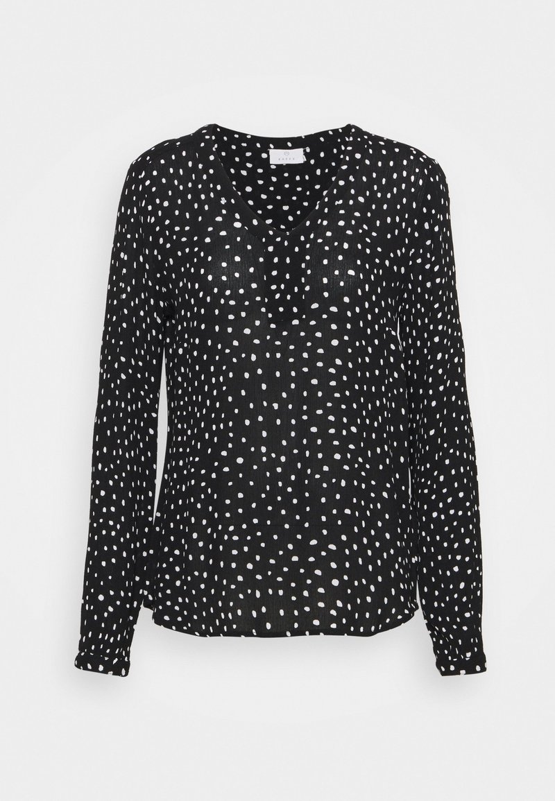 Schwarze Bluse mit langen Ärmeln und V-Ausschnitt, versehen mit einem weißen Punktemuster und einem strukturierten Stoff. Der Saum ist am Boden leicht gekrümmt.