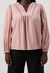 Blusa rosa pallido con scollatura a V e cuciture decorative lungo il colletto. Caratterizzata da maniche lunghe e gonfie e una vestibilità ampia.