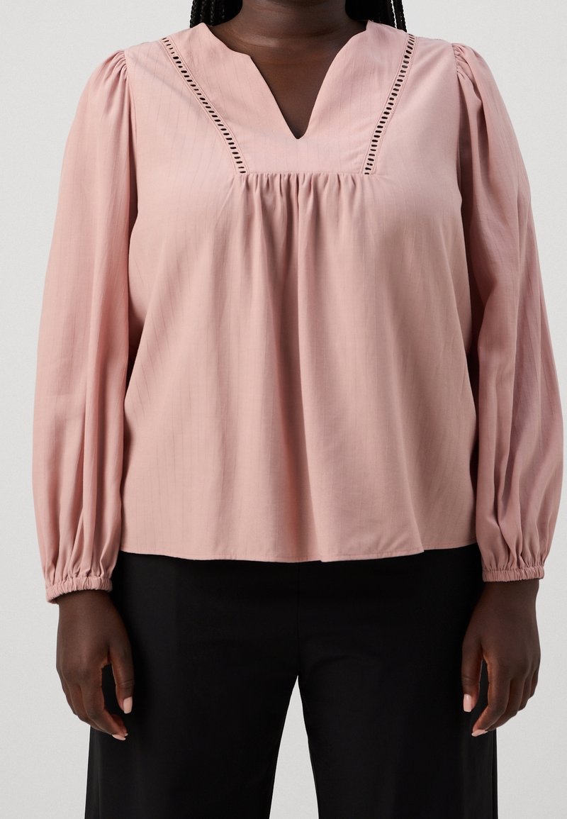 Blusa rosa pallido con scollatura a V e cuciture decorative lungo il colletto. Caratterizzata da maniche lunghe e gonfie e una vestibilità ampia.