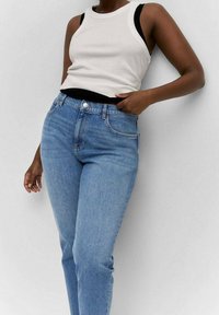 Camiseta sin mangas blanca con ribete en negro, combinada con unos vaqueros de tiro alto en azul claro que presentan un diseño clásico de cinco bolsillos.