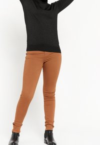 Svart, glittrande polotröja i kombination med figurnära, medelbruna jeans. Modellen bär svarta ankelboots. Enkelt design och enfärgade. 