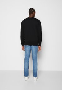 Svart sweatshirt med ribbade muddar och fåll, kombinerad med ljusblå slim fit-jeans och vita sneakers, sedd bakifrån.