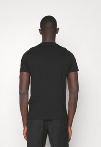 Black short-sleeve t-shirt with a round neck, made from smooth fabric, featuring a subtle brand detail at the hem, shown from the back.