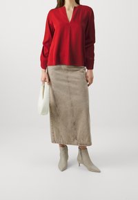 Blusa roja de manga larga con escote en V, combinada con una falda de mezclilla beige y botas ankle beige. Los accesorios incluyen un bolso blanco.