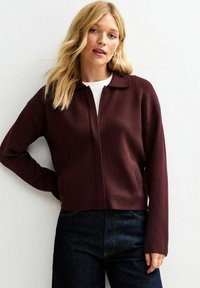 Burgundy zip-up jacket with a collared neck, long sleeves, and textured fabric. Features side pockets and a cropped design.