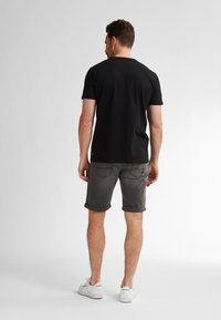 Zwart T-shirt met korte mouwen, gecombineerd met grijze opgerolde shorts en witte sneakers. Het materiaal lijkt zacht; het ontwerp is eenvoudig en casual.