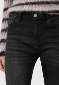 Jeans in denim nero con un design aderente, cinque tasche e chiusura a bottone, caratterizzati da una finitura morbida e leggermente testurizzata.