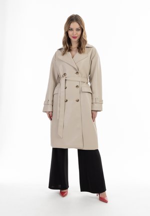 Palton trench bej din piele sintetică, cu un design cu două rânduri de nasturi, nasturi aurii, curea cu fundă și epauleți la umeri. Pantaloni negri cu croială largă și tocuri roșii.