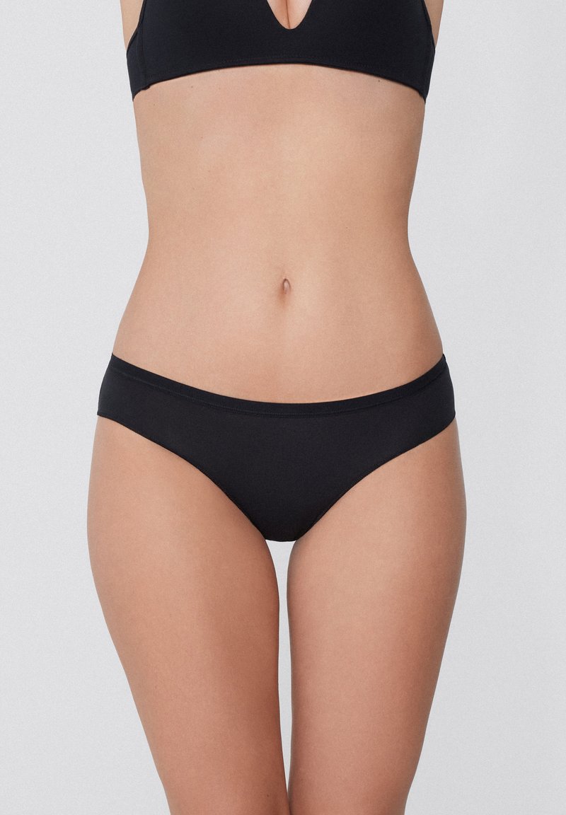 Schwarze Bikini-Unterhose aus glattem Gewebe, mit einem niedrigen Schnitt und minimaler Nahtverarbeitung. Keine zusätzlichen Muster oder Hardware-Details sichtbar.