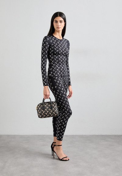 Black long-sleeve fitted top and leggings with silver crescent moon pattern; holding black handbag with gold accents; strappy black high heels.