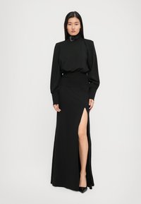 Schwarzes langes Kleid mit tailliertem Bund, hohem Schlitz und langen puffärmel. Verfügt über einen hohen Kragen und strukturierter Stoff. Elegantes Design.