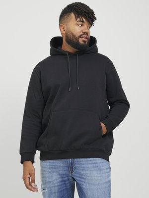 Felpa nera con tasca frontale, cappuccio regolabile con lacci e polsini a costine. Indossata con jeans chiari sbiaditi. Sfondo semplice.